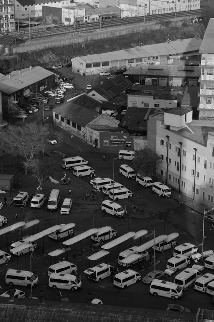 A black and white aerial photograph showing a busy outdoor area adjacent to Uxbridge station, featuring multiple white vans parked on a paved surface during daylight hours. The vans are arranged in ro
